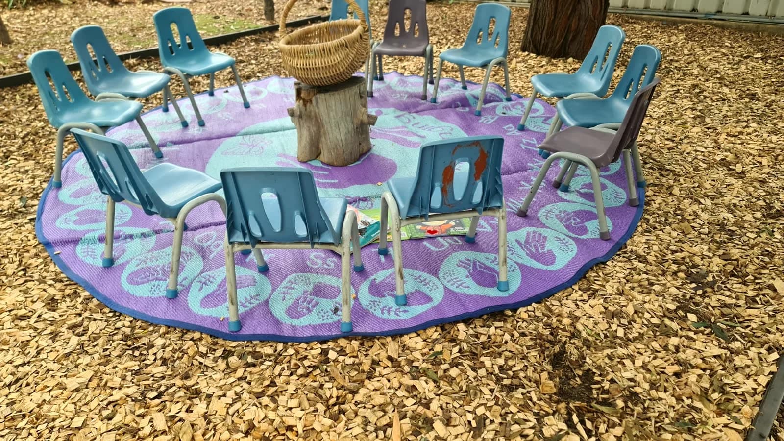 Small colourful chairs arranged in a circle in the centre’s tree-filled yard